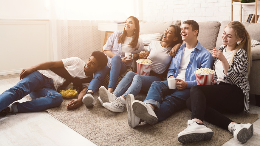 Happy friends watching comedy movie and eating popcorn, sitting on floor at home