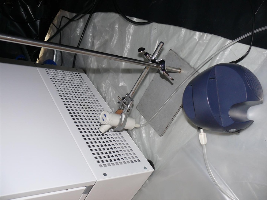 Bild 2 Versuchsaufbau für die „Inaktivierungsanalyse luftgetragener Viren“ in einem Isolatorzelt. Das RNA-Virus MS2 wurde als Surrogat für SARS-CoV-2-Viren als Virussuspension über einen Verneblungskopf (Inhalator) direkt vor der Luftansaugung des AirPurifier-Luftreinigers vernebelt.
