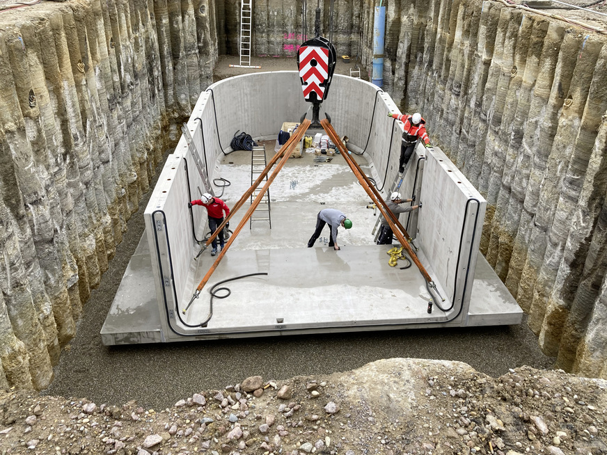 Bild 9 Montage der Betonfertigteile für den thermischen Pufferspeicher auf einer 25 cm starken Schotterschicht mit 5 cm Splittauflage. Der Überstand der Bodenplatte dient der Auftriebssicherung. Die Auflast nach dem Verfüllen der Baugrube wirkt dem Auftrieb des leeren Behälters bei hohem Grundwasserstand entgegen.