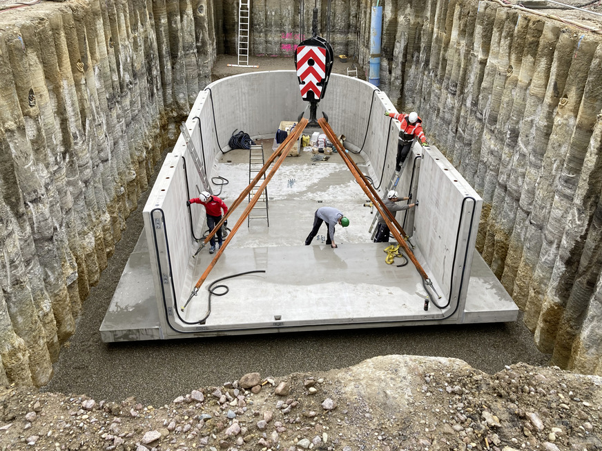 Bild 9 Montage der Betonfertigteile für den thermischen Pufferspeicher auf einer 25 cm starken Schotterschicht mit 5 cm Splittauflage. Der Überstand der Bodenplatte dient der Auftriebssicherung. Die Auflast nach dem Verfüllen der Baugrube wirkt dem Auftrieb des leeren Behälters bei hohem Grundwasserstand entgegen.