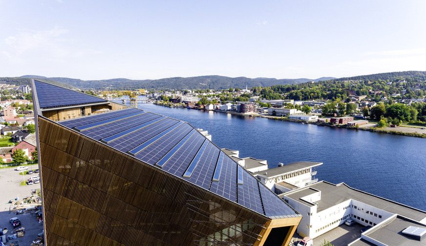 Das stark geneigte Dach ist fast vollständig mit Photovoltaik-Panels belegt. Lichtbänder mit Oberlichtern dienen der Belichtung der Tagungsräume darunter.