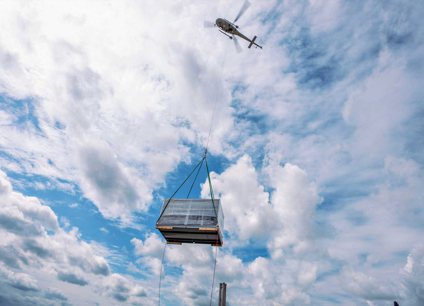 Air-Logistik: Am 30 m langen Seil transportiert ein Helikopter die Klimageräte auf der letzten Meile in die Therme Erding.