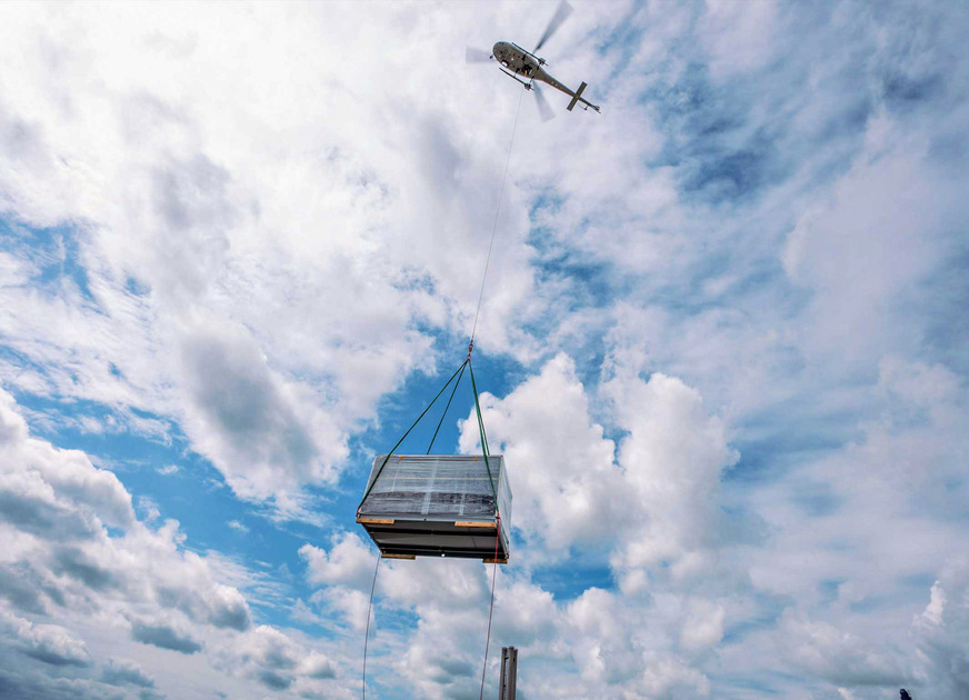 Air-Logistik: Am 30 m langen Seil transportiert ein Helikopter die Klimageräte auf der letzten Meile in die Therme Erding.
