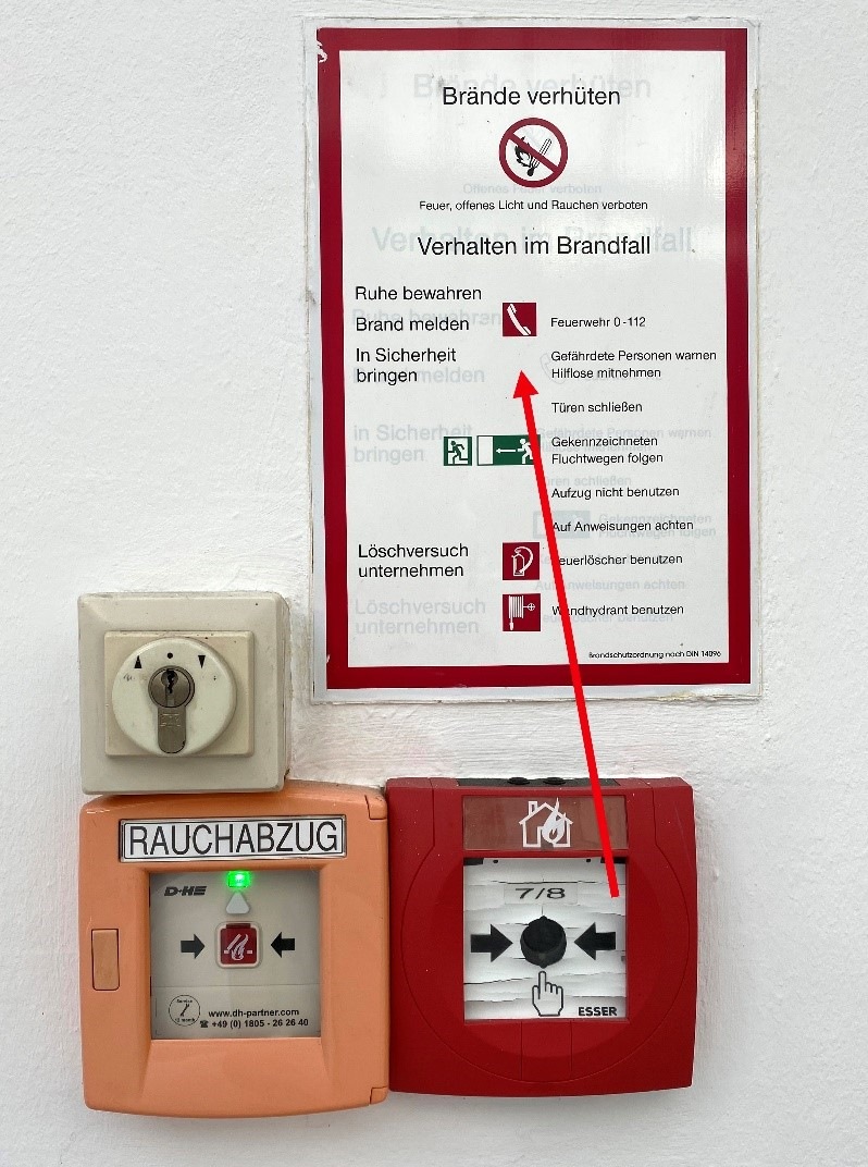 Negativbeispiel: Handfeuermelder ist vorhanden – Hinweis in der BSO „Handfeuermelder betätigen“ und Brandschutzzeichen F005 fehlen.