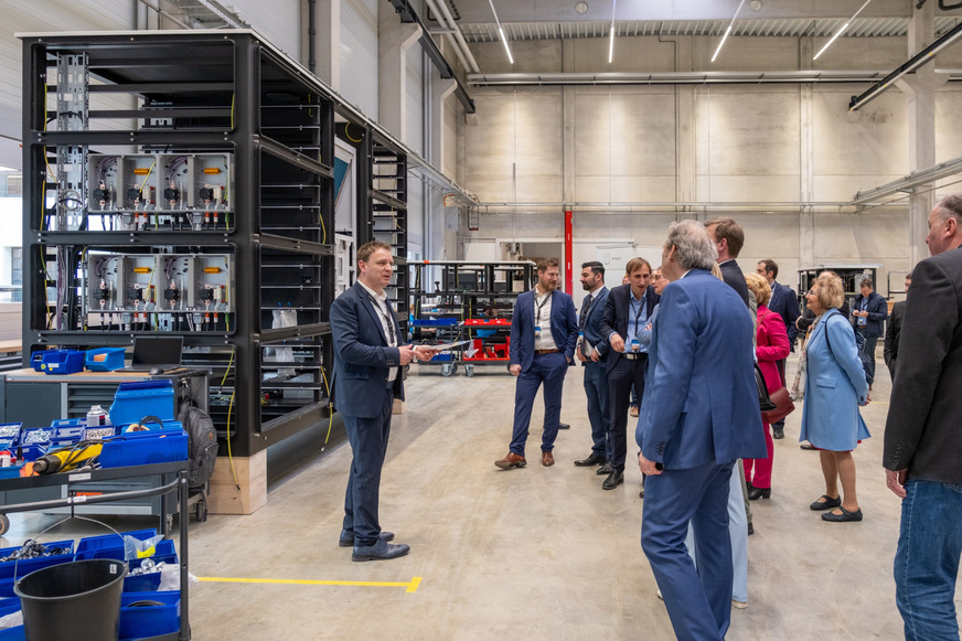 Bild 2 Im April 2024 ist die CarBatteryReFactory von Fenecon in Iggensbach im Landkreis Deggendorf offiziell in Betrieb gegangen. In der „große Produktionshalle“ entstehen jährlich bis zu 500 Gewerbe- und Industriespeicher mit Kapazitäten von 82 bis 1288 kWh und flüssigkeitsbasiertem Thermomanagement. Dabei kommen ausschließlich neue Elektroautobatterien von deutschen Premium-Fahrzeugherstellern zum Einsatz. Franz-Josef Feilmeier (links), Gründer und Geschäftsführer von Fenecon, führt Gäste bei der Eröffnung Ehrengäste durch das neue Werk.