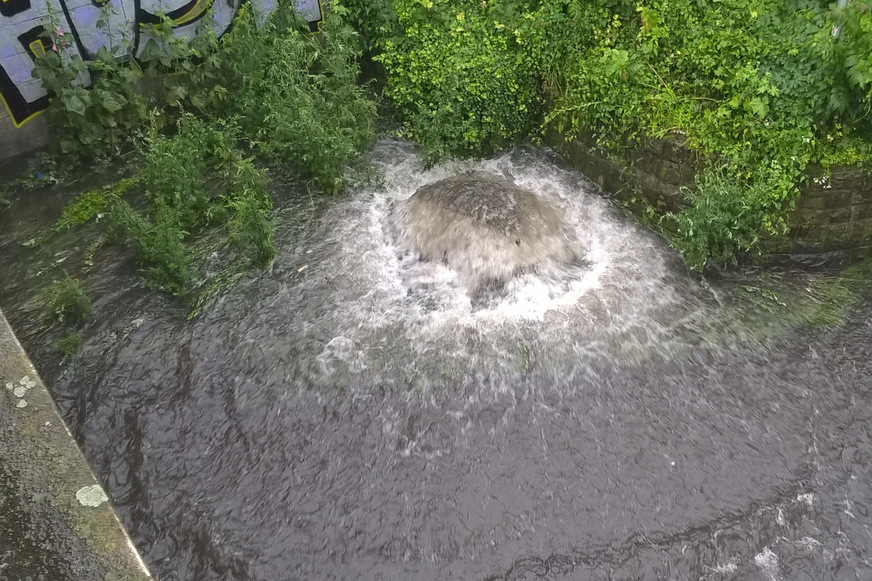 Bild 7 Wasser quillt aus einer Schachtabdeckung. Die Ursache ist üblicherweise Rückstau aus dem Kanal als Folge eines Starkregenereignisses. Bei unterirdischen Regenwasserspeichern unterhalb der Rückstauebene, die nicht gegen Rückstau gesichert sind, droht die Kontamination des Wasservorrats.