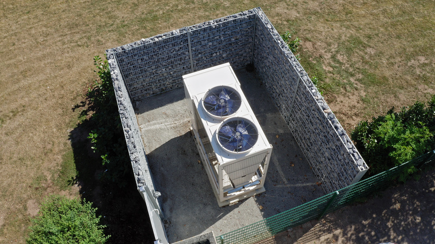 Aus Sichtschutzgründen von Gabionen umgeben, befindet sich die Luft-Wasser Wärmepumpe Aerotop® L65 von ELCO in der Grünanlage zwischen zwei der vier Häuser.