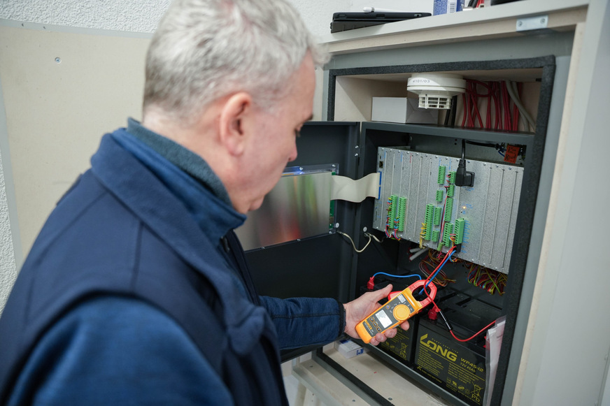 Bild 2 Ein TÜV-SÜD-Sachverständiger prüft die Brandmelderzentrale auf Alarm- und Ruhestrom, Um sicherzustellen, dass die Batterien bei Stromausfall die Funktionsfähigkeit der Anlage gewährleisten. Bei der Energieversorgung bestehen oft Mängel.