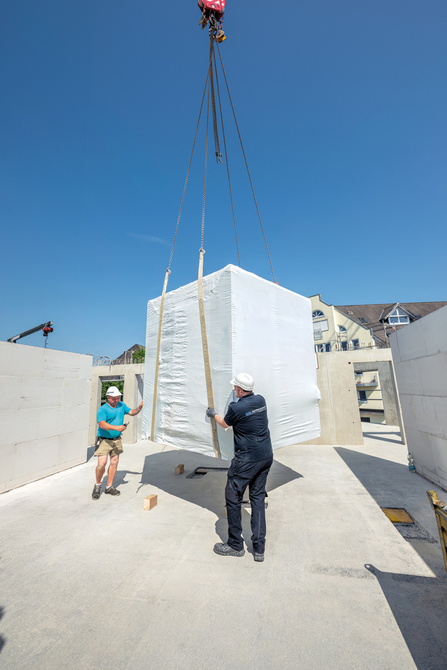 Monteure nehmen das vorgefertigte Badmodul vom Kran an und bereiten das Einsetzen in den Rohbau vor.