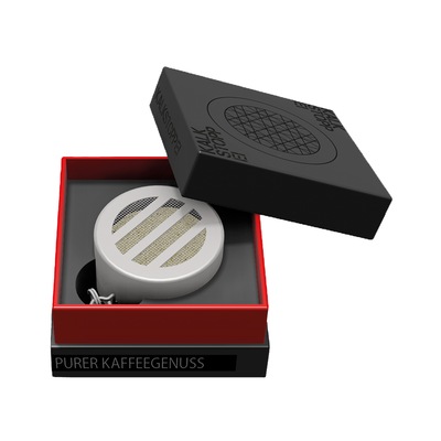 Ein rundes, weißes Gerät in einer offenen schwarz-roten Schachtel mit der Aufschrift "PURER KAFFEEGENUSS.