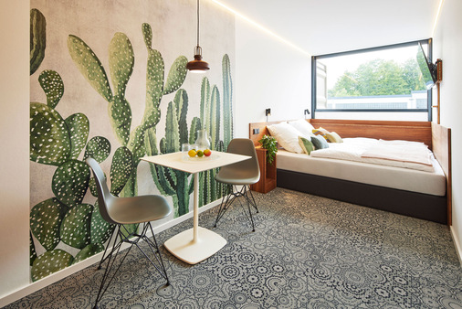  Originelle Wandgestaltungen und eine voll verglaste Außenwand für viel Tageslicht sind gemeinsame Merkmale der Containerzimmer in einem TIN INN Hotel.