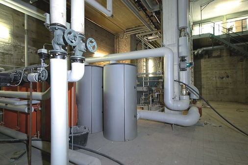 Die Zeit verändert: In dem scheunengroßen Heizungskeller, wo vor Jahren noch zwei riesige Ölkessel standen, genügen heute zwei 750-l-Pufferspeicher dafür, die Spitzenlast des ansonsten direkt über Fernwärme und Plattenwärmeübertrager in den Hauswasserstationen abgedeckten Raumwärmebedarfs aufzufangen.