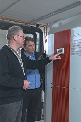 Bauherr Udo Hack lässt sich von Manfred Hoppen, Inhaber der ausführenden Firma Klein, die Funktionen der Wärmepumpenregelung erläutern. Die Wärmepumpe mit Umschaltung auf passives Kühlen, stellt eine Heiz-leistung von bis zu 96,3kW zur Verfügung. Durch die optimierte Auslegung wird eine Jahresarbeitszahl von über 4,7 auf Basis der VDI4650 erreicht, sodass die Voraussetzungen zur Inanspruchnahme der Innovations­förderung des Marktanreizprogramms erreicht wurden.