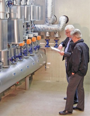Abb. 2 KSB-Planerberater Joachim Traum (links) und Fachplaner Dipl.-Ing. (FH) Markus Albert an der neu aufgebauten Heizungsverteilung. Zur Optimierung der Wärmeverteilung wurden drehzahlgeregelte Hocheffizienz-Umwälzpumpen Rio-Eco zusammen mit dem KSB-Regelsystem BOA-Systronic mit mengenvariabler Beimisch­haltung eingesetzt.