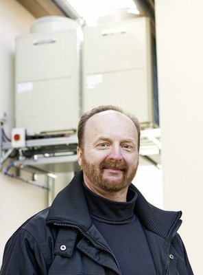 Abb. 4 Frank Lubich vor dem VRF-Außengerät, das in einem Versorgungsgang untergebracht wurde: „Durch die Wärme- und Kälterück­gewinnung des integrierten Lossnay-Geräts ­konnten die Innen- und Außeneinheiten kleiner dimensioniert werden.“