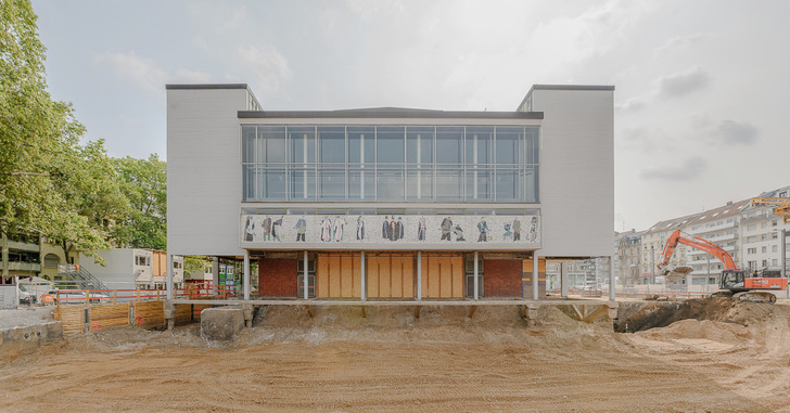 Ein modernes, im Bau befindliches Gebäude mit Kunstwerken von Menschen über versperrten Erdgeschoss-Eingängen. - © Maximilian Borchardt