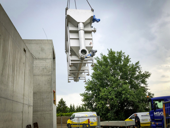 Bild 1 Lieferung der beiden Abwasser/Wasser-Wärmeübertrager. Links der Anbau des neuen Rathauses von Schallstadt mit der Heizzentrale des kalten Nahwärmenetzes. Hier begegnen sich der warme Primärkreislauf mit Abwasser und der kältere Sekundärkreislauf des Wärmenetzes. - © Energiedienst / Junkov
