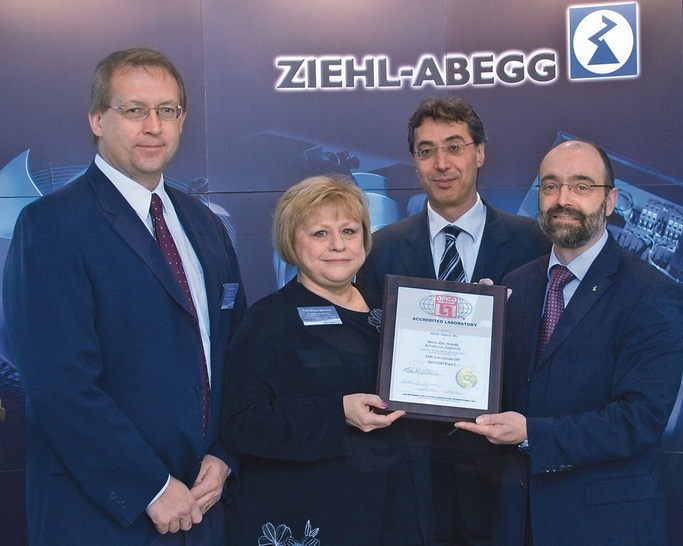 Mark Stevens, AMCA Deputy Executive Director, Technical ­Affairs, (links) und Barbara Morrison, AMCA CEO, überreichen Norbert Schuster, Mitglied des Vorstandes bei Ziehl-Abegg (rechts) und Dr. Omar Sadi, technischer Leiter für Lufttechnik bei Ziehl-Abegg, die Akkreditierungs-Urkunde.