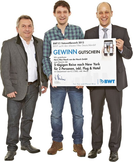 Siegerehrung: Herbert Schüssel, BWT-Verkaufsberater München, (links) und Andreas Milich, BWT-Gebiets­vertriebsleiter Süd, (rechts) übergeben Max Hauck den Reisegutschein nach New York für sein Siegerfoto.
