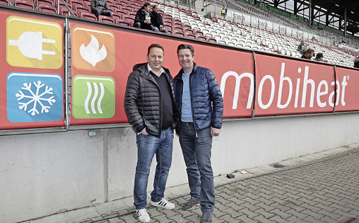 



Die mobiheat-Firmen-gründer Helmut Schäffer (links) und Andreas Lutzenberger präsentieren die Bandenwerbung in der WWK Arena in Augsburg. 
