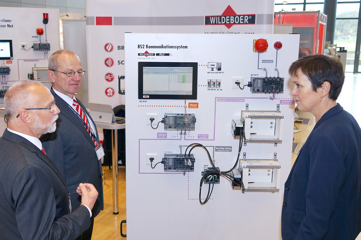 Klaus Gebert (links) und Gerhard Stelzer, beide Mitarbeiter Technik und Vertrieb bei Wildeboer, übergeben die Musterwand mit dem Wildeboer-Net an Dipl.-Ing. Cynthia Tschentscher, Leiterin der Produktgruppe Brandschutz bei Eipos.