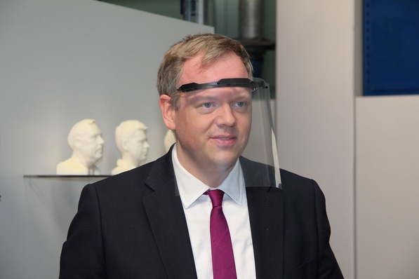 Landrat Dr. Matthias Neth probiert gleich einen Gesichtsschild aus, der aus einem 3D-gedruckten Träger, einer Tageslichtprojektorfolie und Gummiband besteht.
