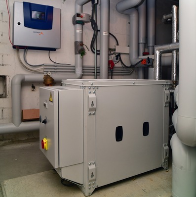 eXergiemaschine mit Regelung (an der Wand). Die spezielle Wasser/Wasser-Wärmepumpe arbeitet in Kombination mit einem Pufferspeicher, der gleichzeitig Wärmequelle- und Wärmesenke ist.