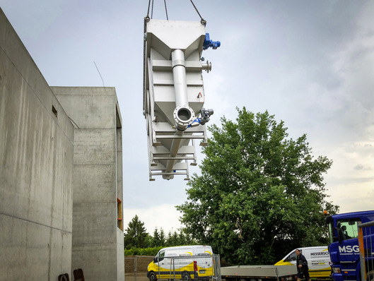 Bild 1 Lieferung der beiden Abwasser/Wasser-Wärmeübertrager. Links der Anbau des neuen Rathauses von Schallstadt mit der Heizzentrale des kalten Nahwärmenetzes. Hier begegnen sich der warme Primärkreislauf mit Abwasser und der kältere Sekundärkreislauf des Wärmenetzes.