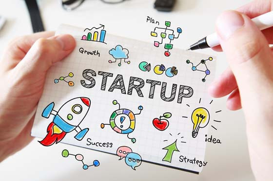 Mans hand drawing Startup concept on white notebook