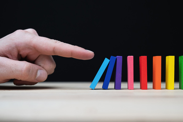 Alt-Text: „Symbolische Darstellung der digitalen Vernetzung in der Gebäudetechnik durch das Anstoßen einer Reihe farbiger Dominosteine, die innovative Technologien und integrierte Systeme repräsentieren. - © Martin – stock.adobe.com