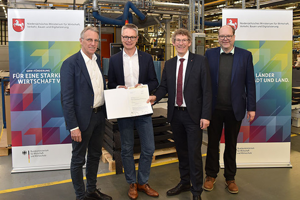 Alt-Text: „Vier Fachleute in Geschäftskleidung diskutieren ein Dokument zu digitalen Gebäudetechnologien vor Bannern und moderner Gebäudeausrüstung im Hintergrund. - © Stiebel Eltron