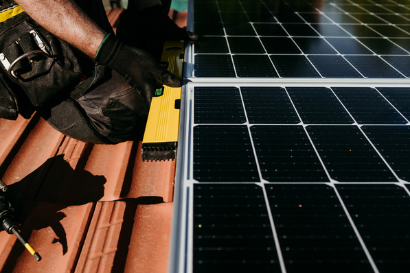„Ingenieur justiert Photovoltaikmodule auf einem Gebäude, konzentriert auf optimale Ausrichtung für dezentrale Energieerzeugung und intelligente Netzwerkintegration. - © Eva - stock.adobe.com