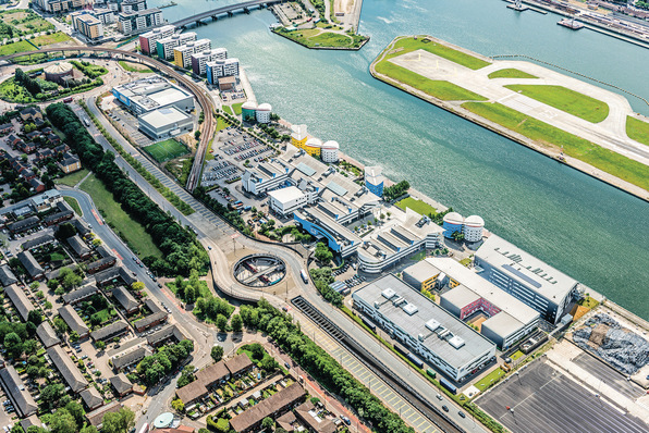 Luftaufnahme einer urbanen Flusslandschaft mit modernen Gebäudekomplexen, integrierten grünen Flächen und Straßeninfrastruktur, die eine zukunftsweisende Smart-Building-Architektur sowie Konzepte der dezentralen Energieerzeugung und des intelligenten Energiemanagements veranschaulicht. - © University of East London