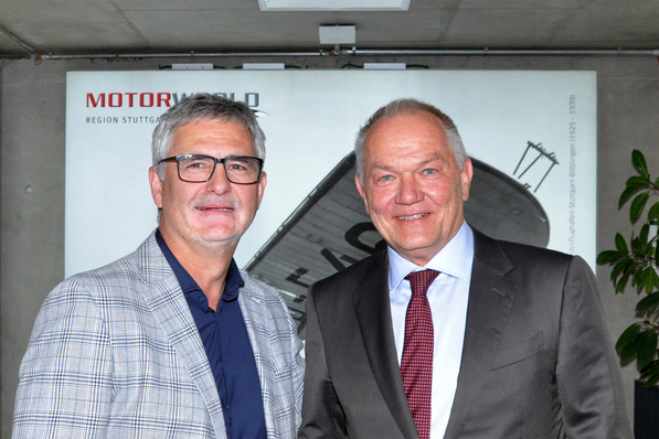Hier ist ein optimierter, fachlich relevanter Alt-Text für Ihre Zielgruppe und Themen: Alt-Text-Vorschlag: „Zwei Fachplaner im Anzug stehen bei einem Branchenevent vor dem MOTORWORLD-Schriftzug und diskutieren über Digitalisierung und Gerne intelligente Gebäudetechnik.“ Alternative ausführlichere Variante: „Zwei TGA-Experten in Businesskleidung tauschen sich auf einer Branchenveranstaltung vor dem MOTORWORLD-Logo über innovative Lösungen zu Digitalisierung, Smart Building-Technologien und Energiemanagement aus.“. - © ja / BTGA